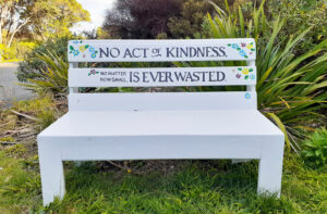 White painted bench seat in a grassed area. The words "No act of kindness, no matter how small, is ever wasted".