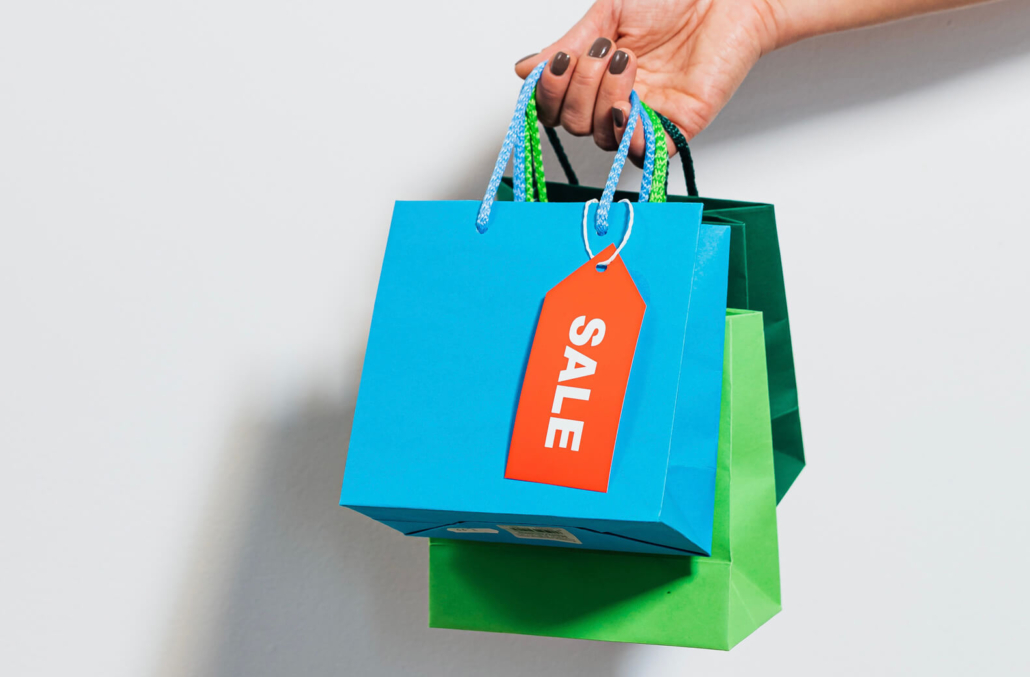 A hand holding colourful paper shopping bags on a white background