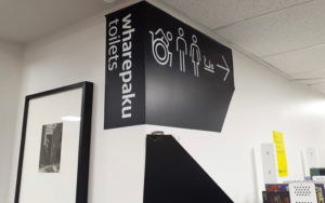 Black panel painted on a white wall with the words wharepaku toilets and some toilet icons