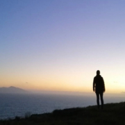 Silhouette of person looking out to sea from a clifftop at dawn